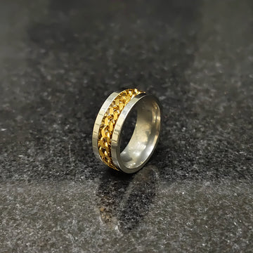 Golden curb chain ring for men in pakistan with silver band on dark textured surface