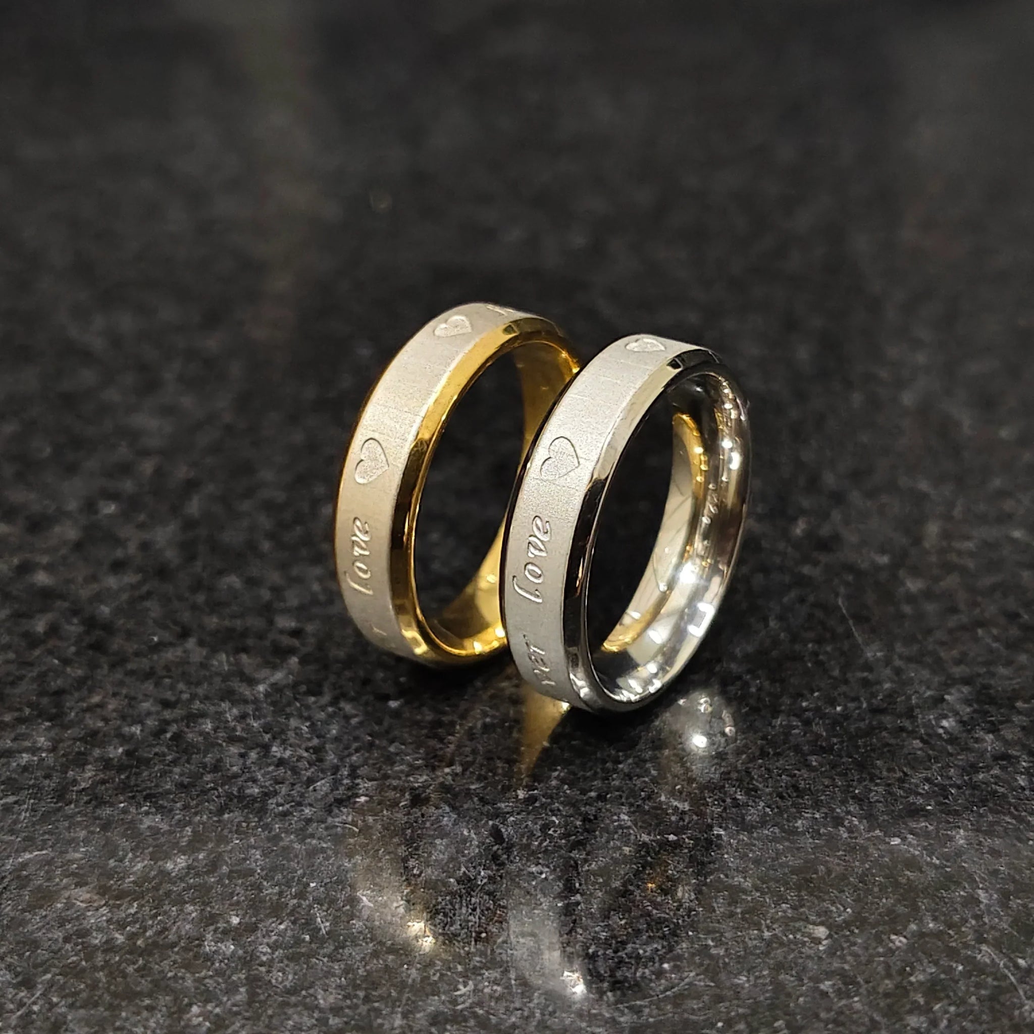 Lamha 2 forever love rings for men with heart and love engravings in gold and silver tones on black stone background