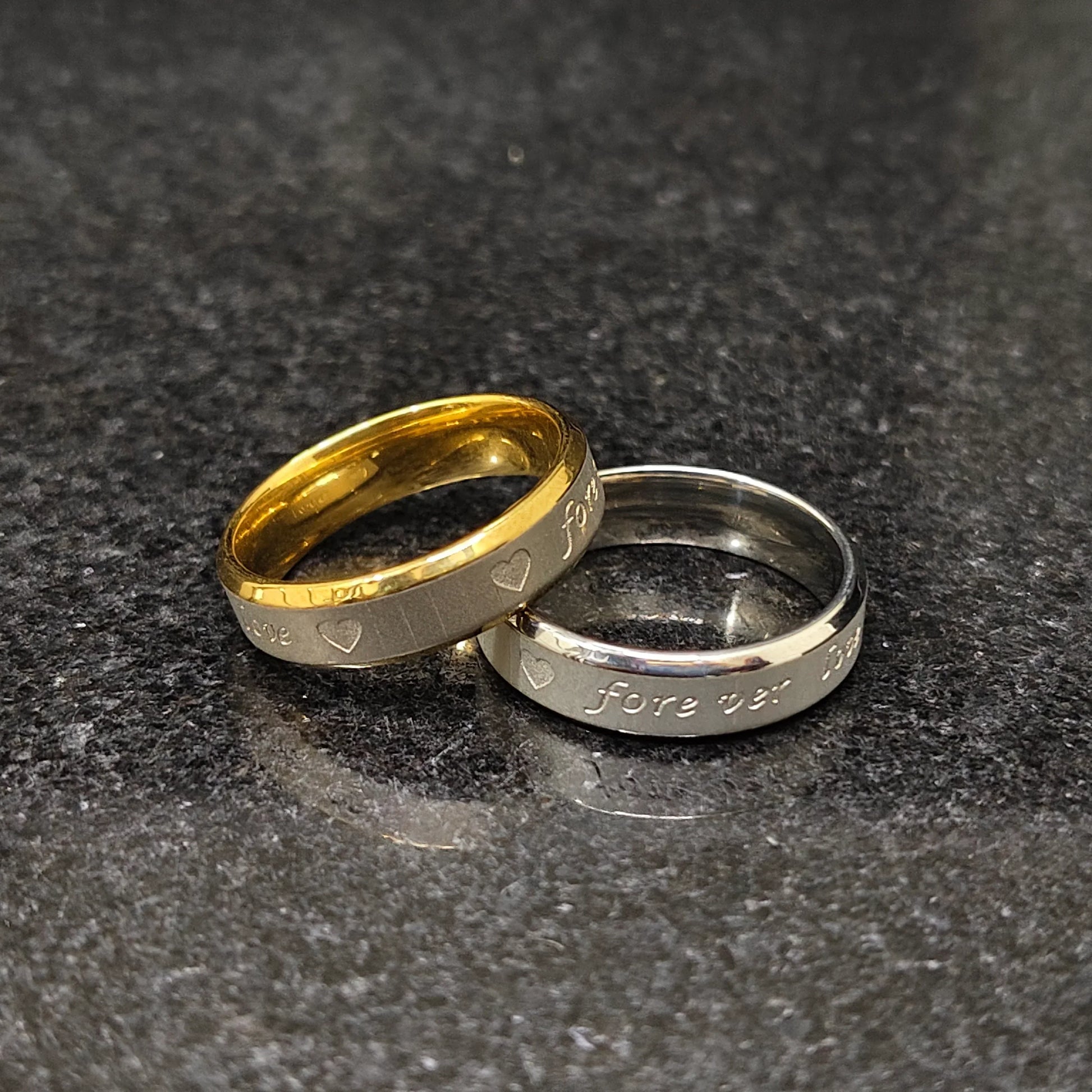 Lamha 2 forever love rings for men with heart engravings in gold and silver finish on dark surface
