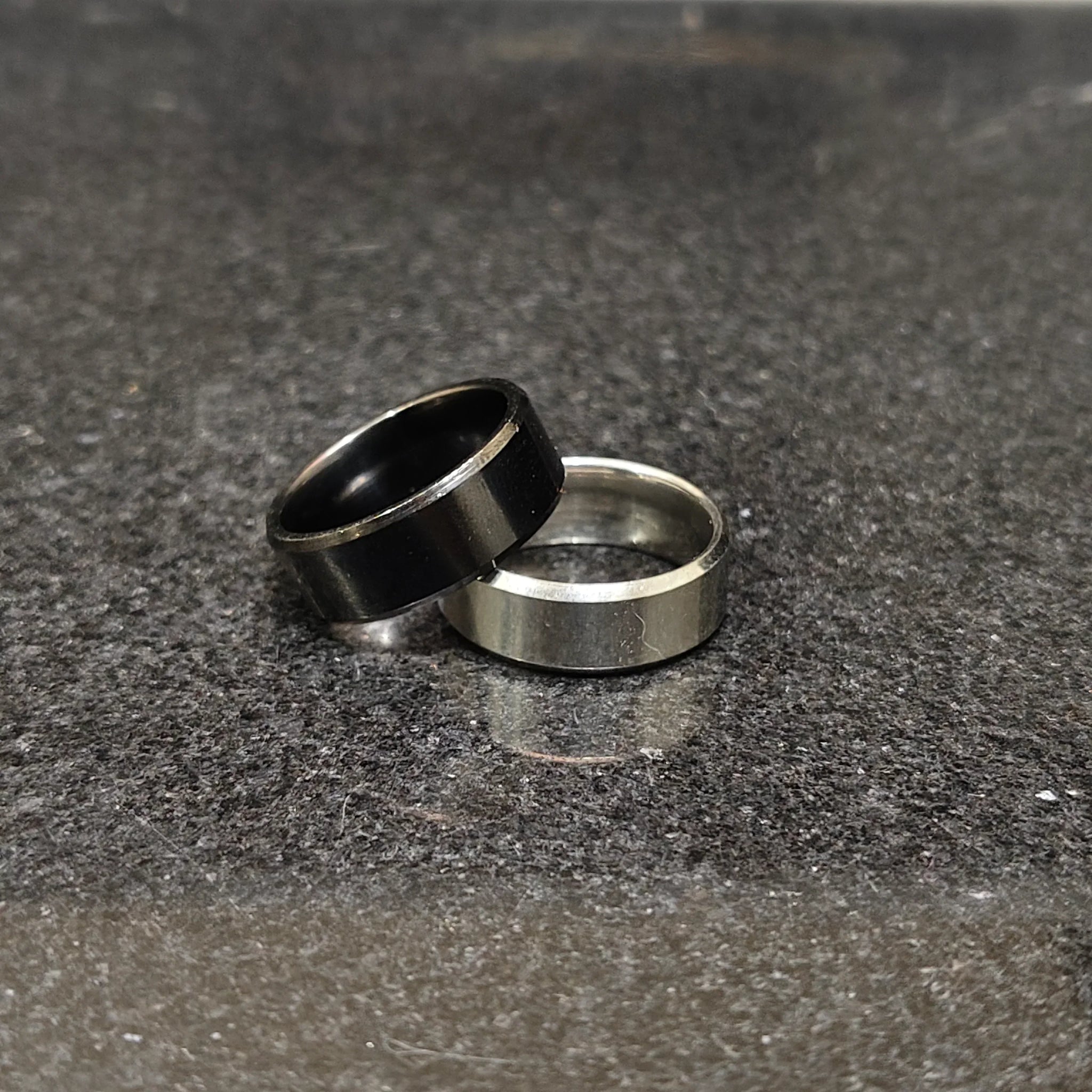2 rings black and silver for men in pakistan with simple modern design on dark textured surface