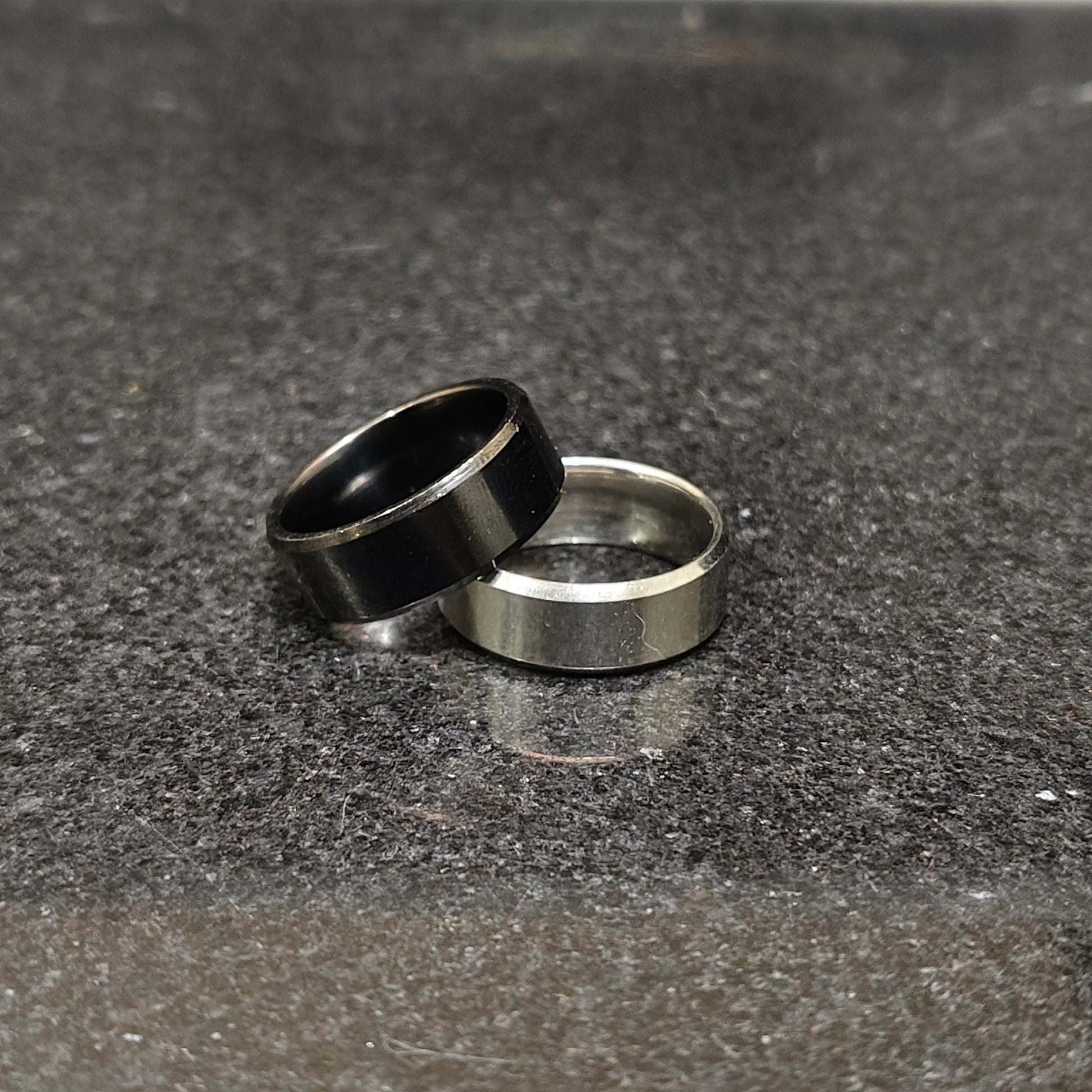 2 rings black and silver for men in pakistan with simple modern design on dark textured surface