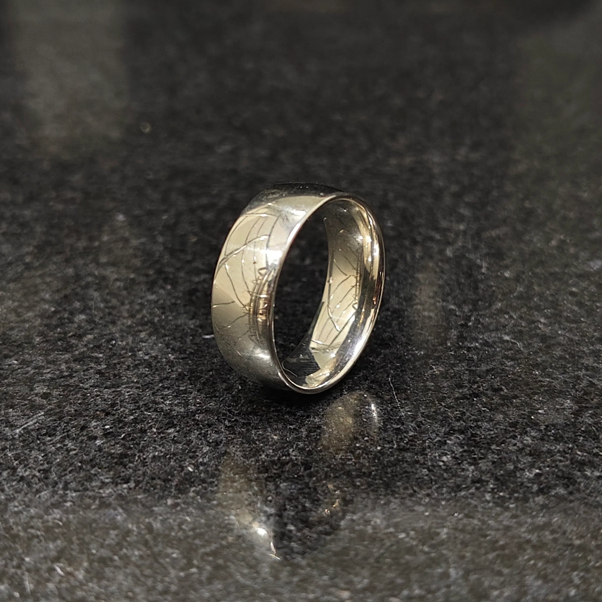 Classic silver ring for men with a smooth polished finish on a dark reflective surface