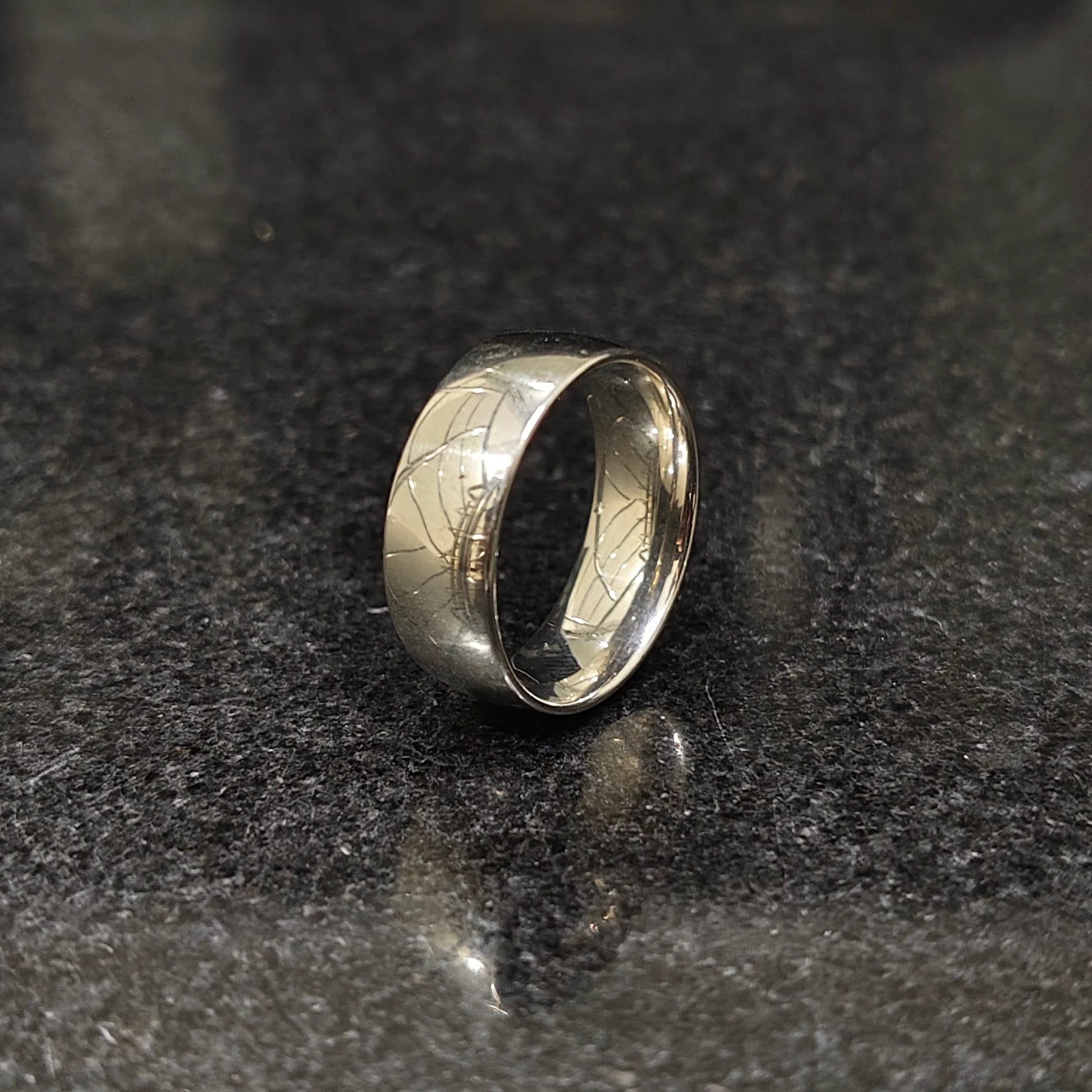 Classic silver ring for men with a smooth polished finish on a dark reflective surface