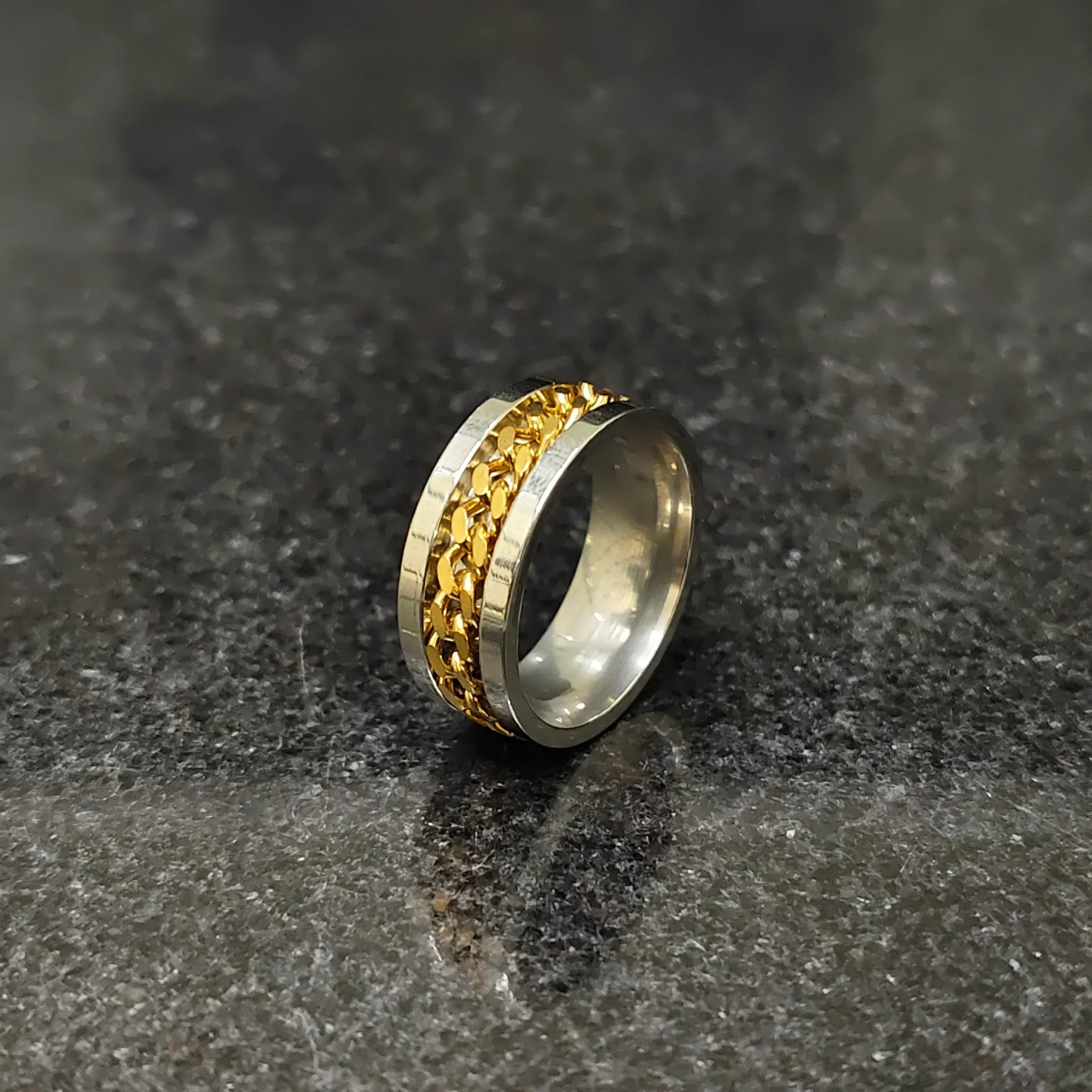 Golden curb chain ring for men in pakistan with silver band on dark textured surface