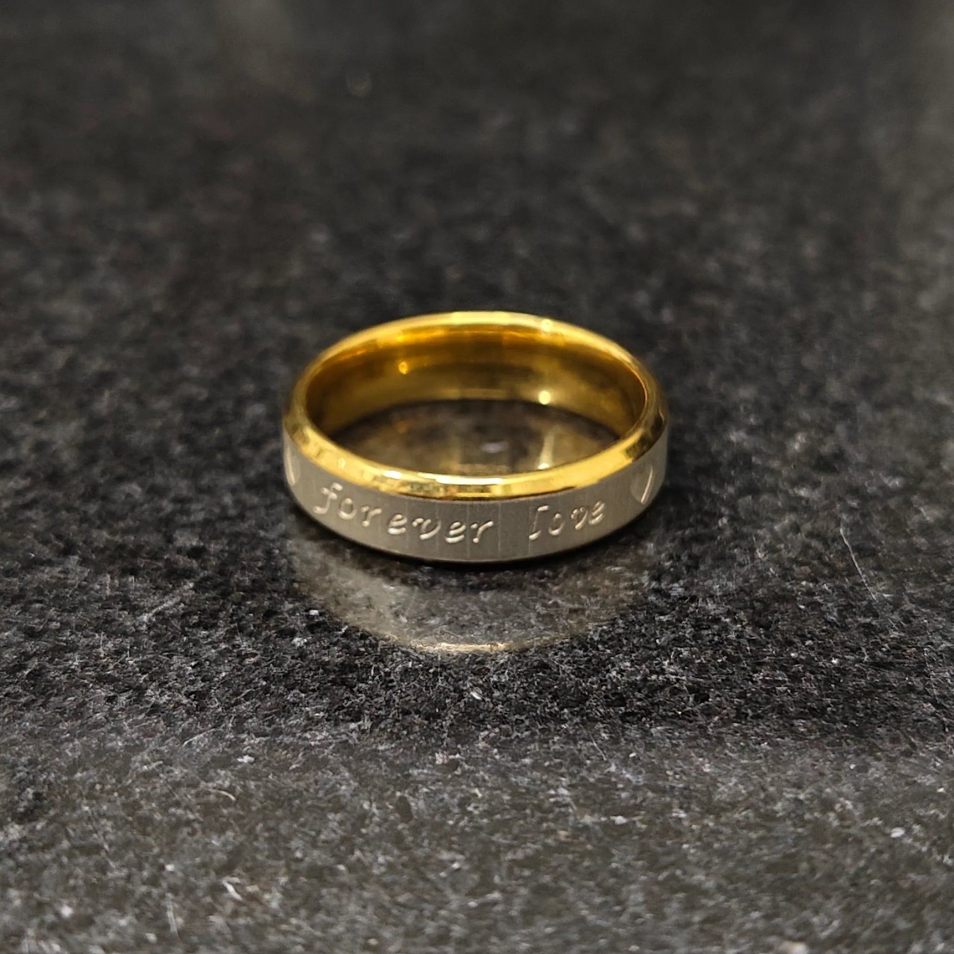 Love ring for men in golden forever color with engraved forever love text on a dark surface