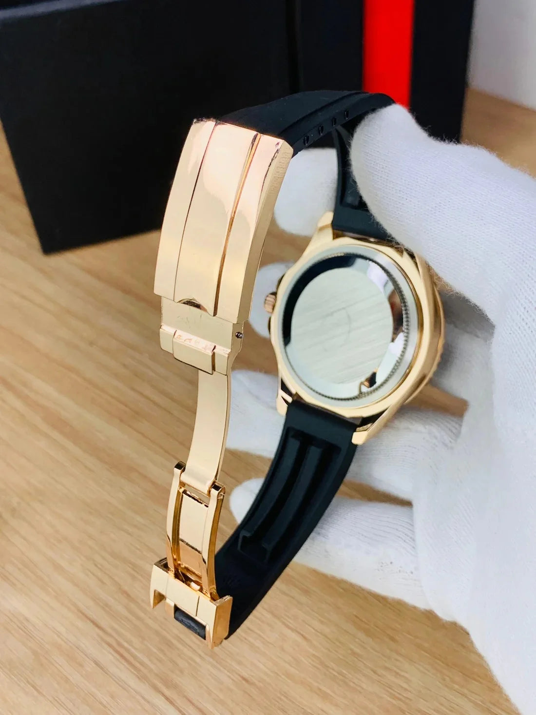 Rose gold black Rolex watch for men with black rubber strap held by gloved hand