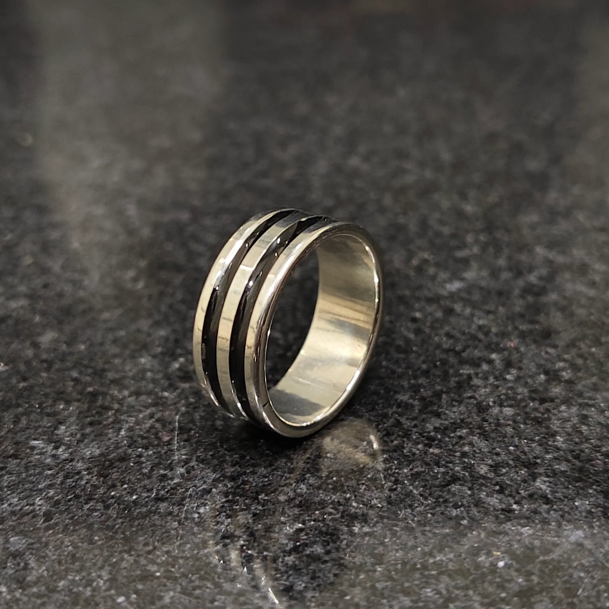 Silver black line ring for men in best design with a polished finish on a dark granite surface