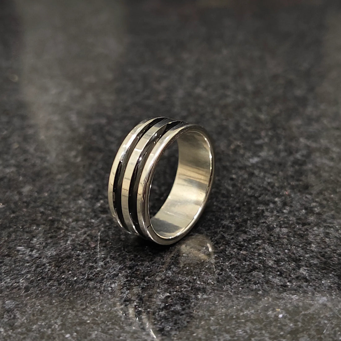 Silver black line ring for men in best design with a polished finish on a dark granite surface