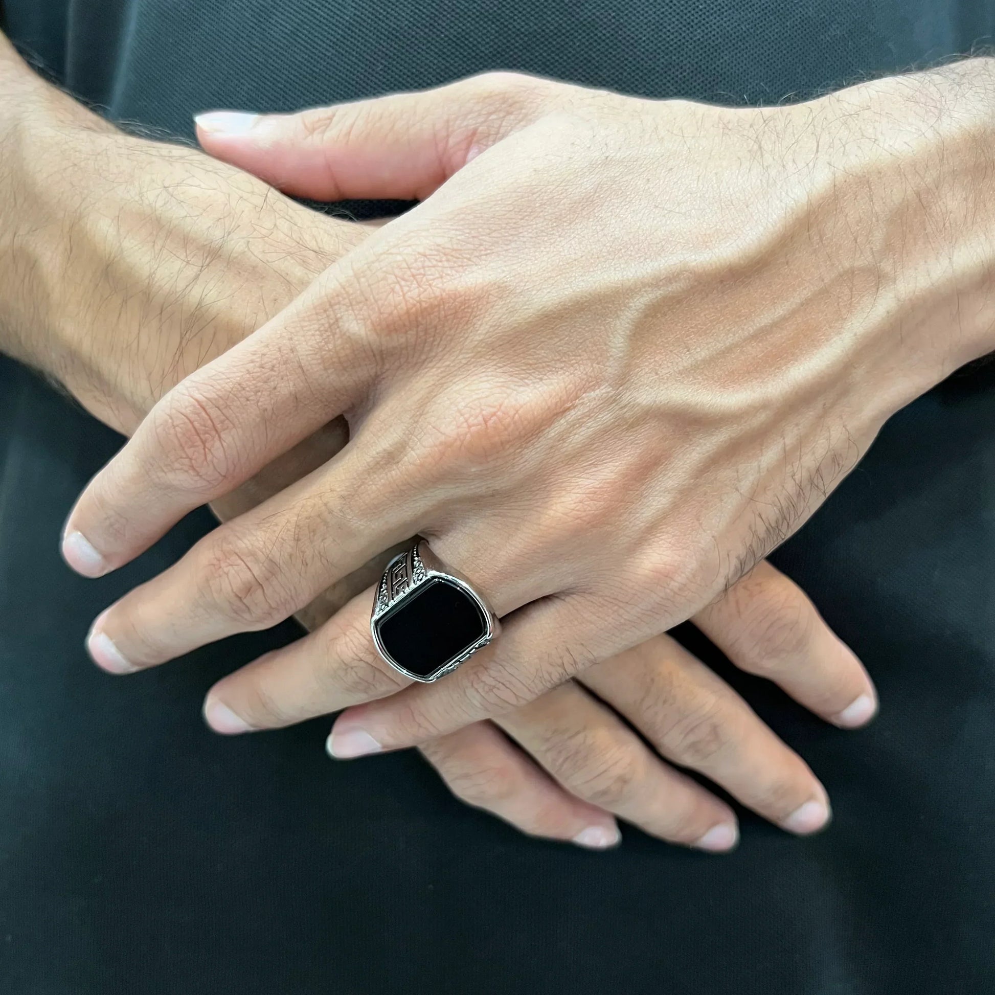 Close-up of hands wearing Lamha silver medusa stone rinf or men with black stone and detailed silver band