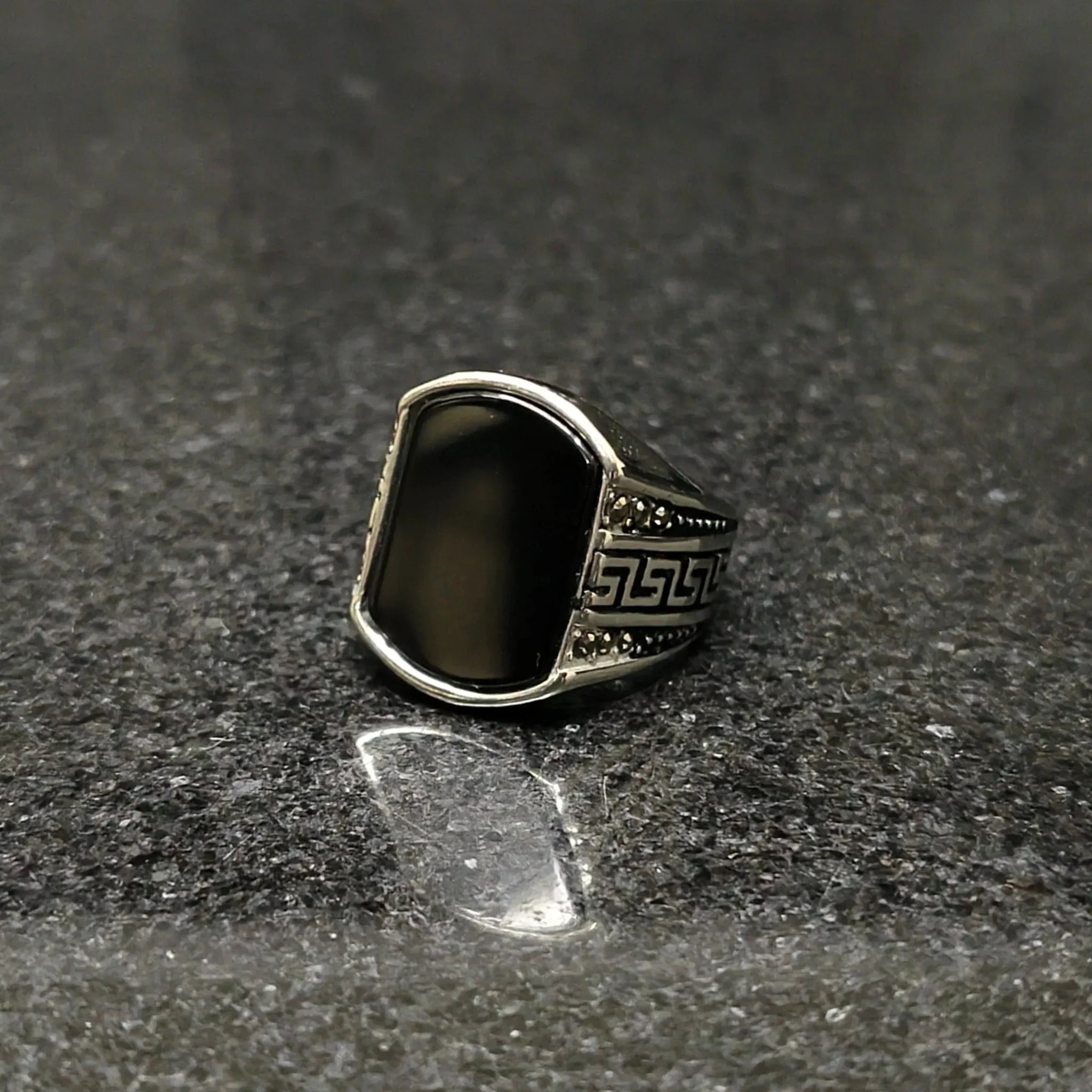 Silver Medusa stone rinf or men with black stone and intricate side carvings on dark surface
