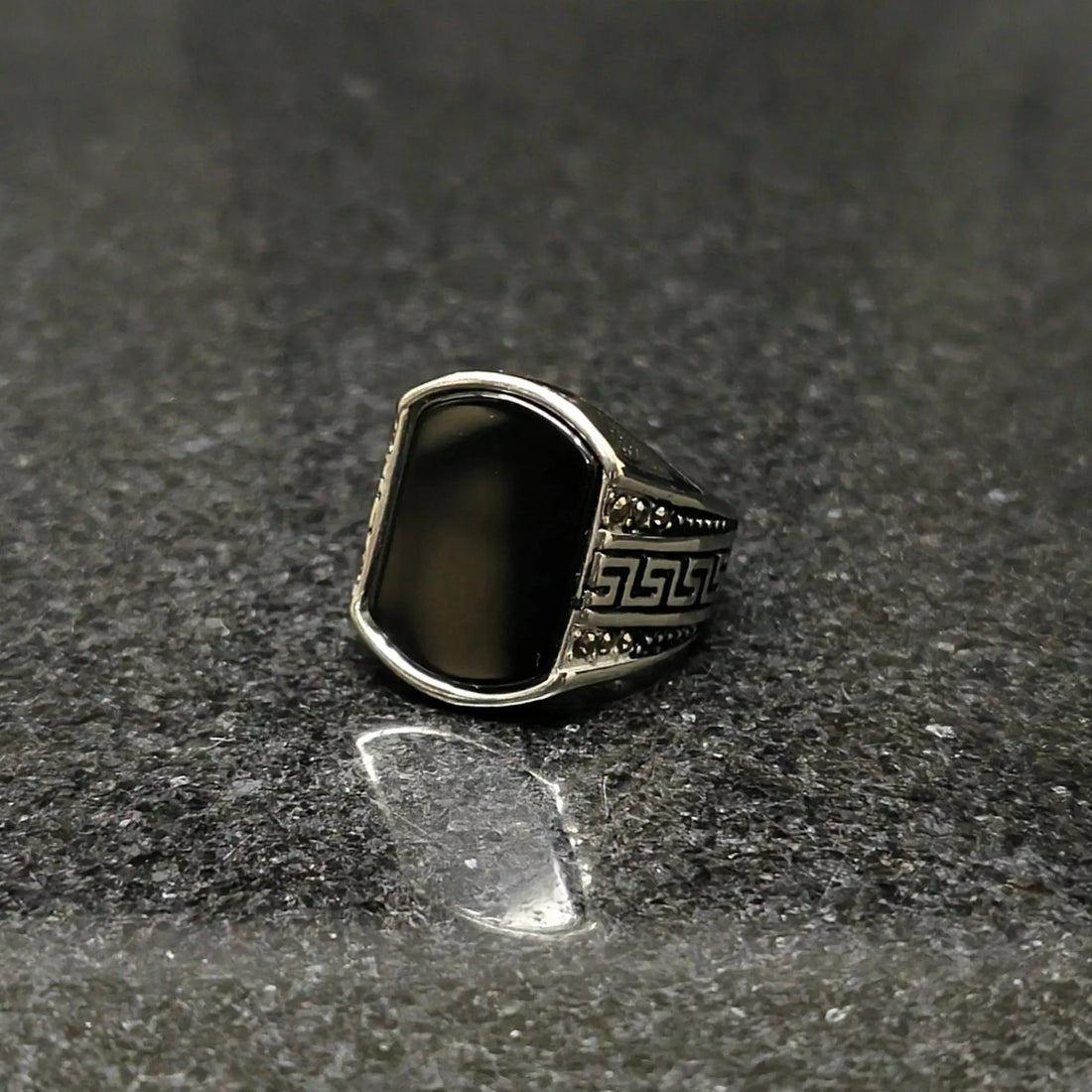 Silver Medusa stone rinf or men with black stone and intricate side carvings on dark surface