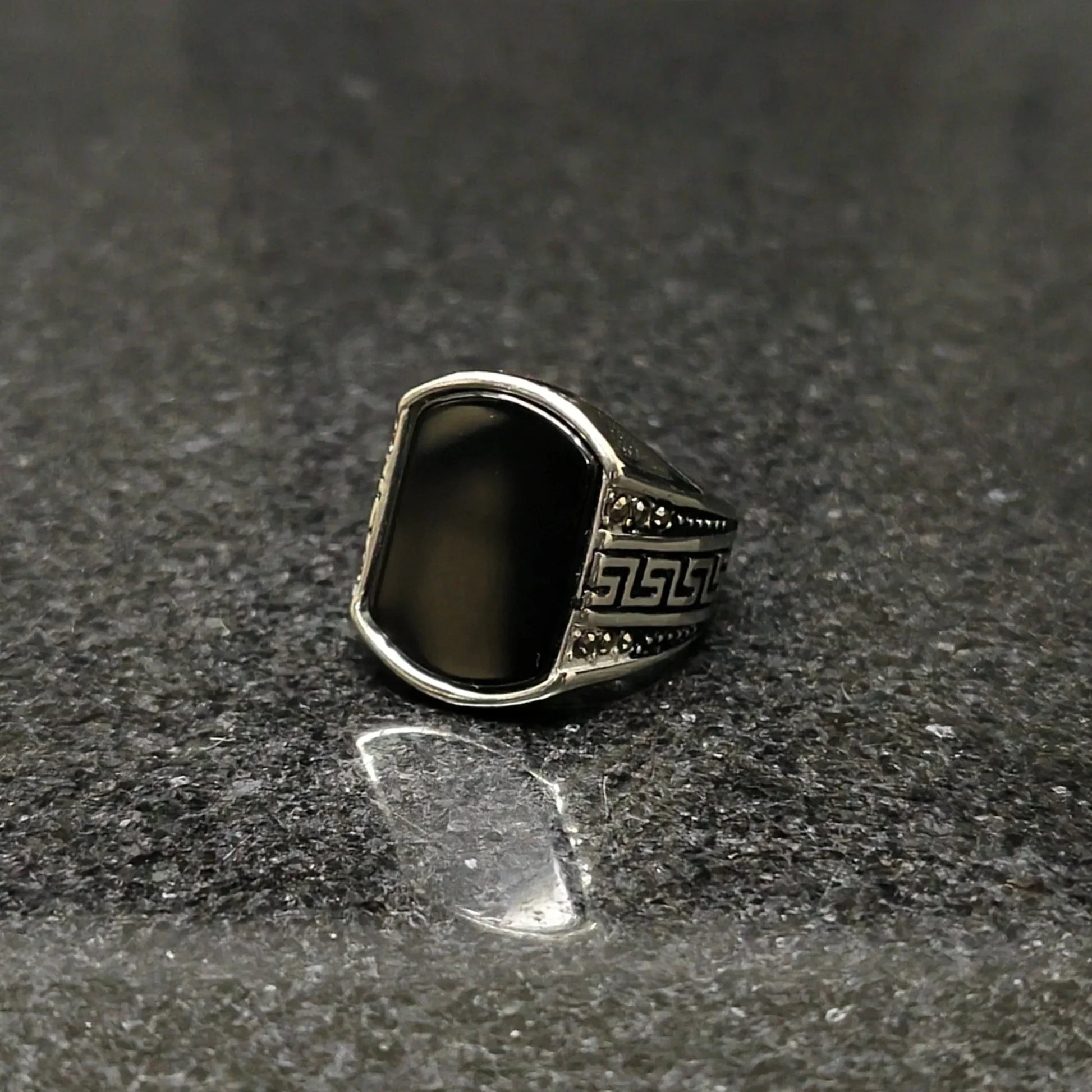 Silver Medusa stone rinf or men with black stone and intricate side carvings on dark surface