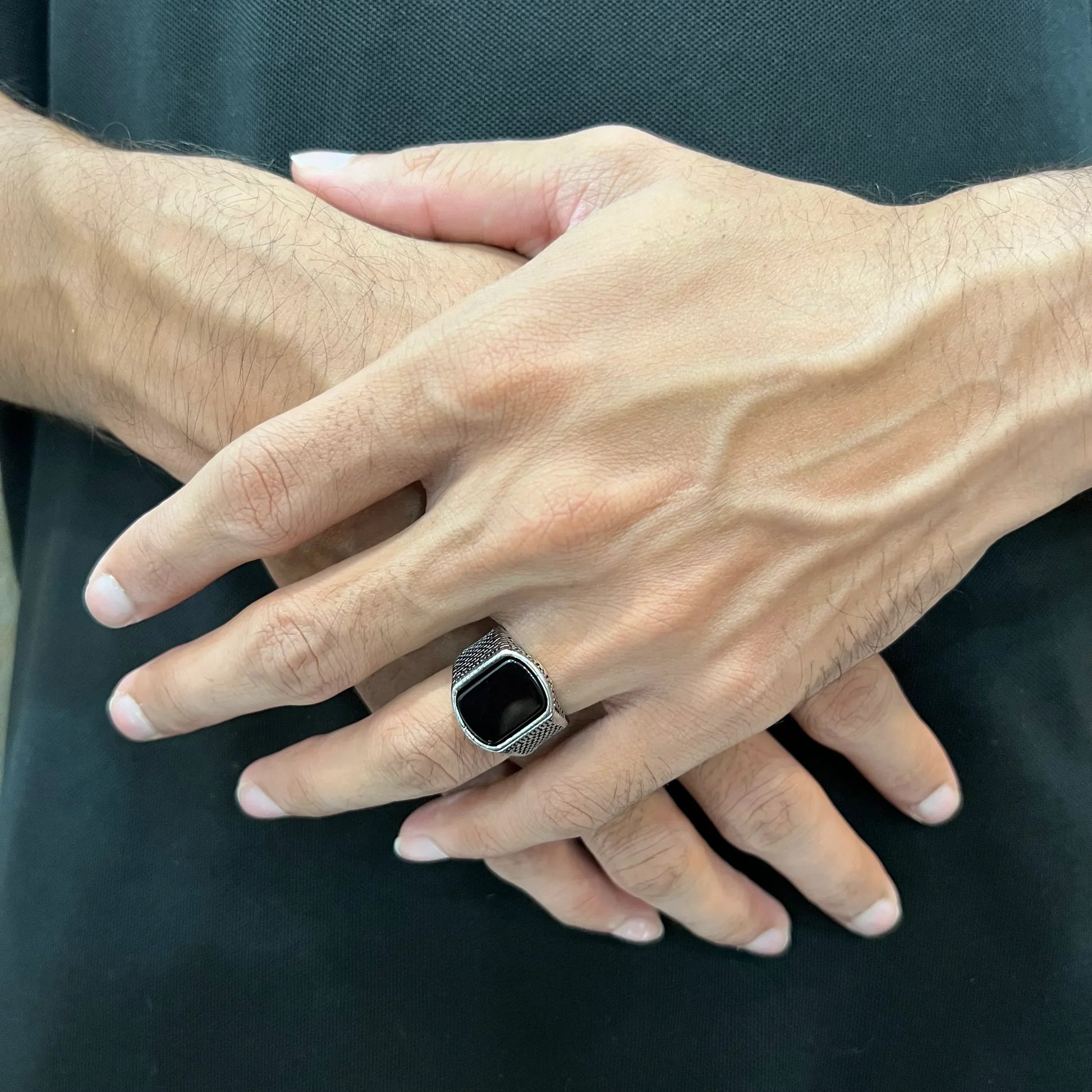 Silver retro ring for men with black stone worn on hand over black shirt background